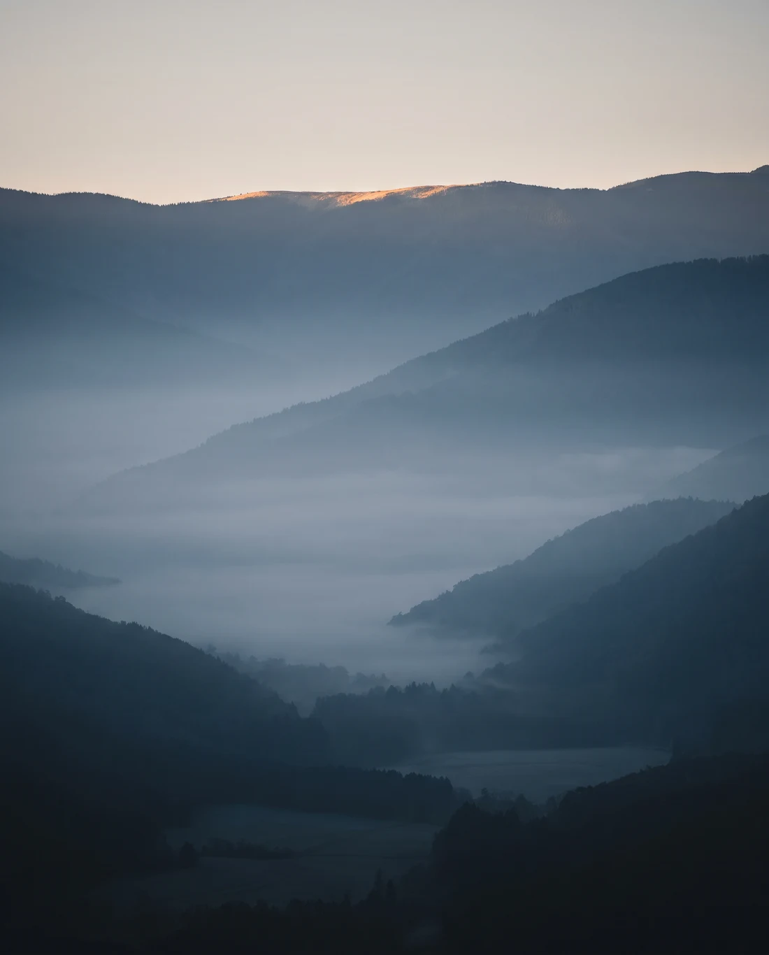 A quiet valley in blue shadow at dawn, with first light along the far ridge.