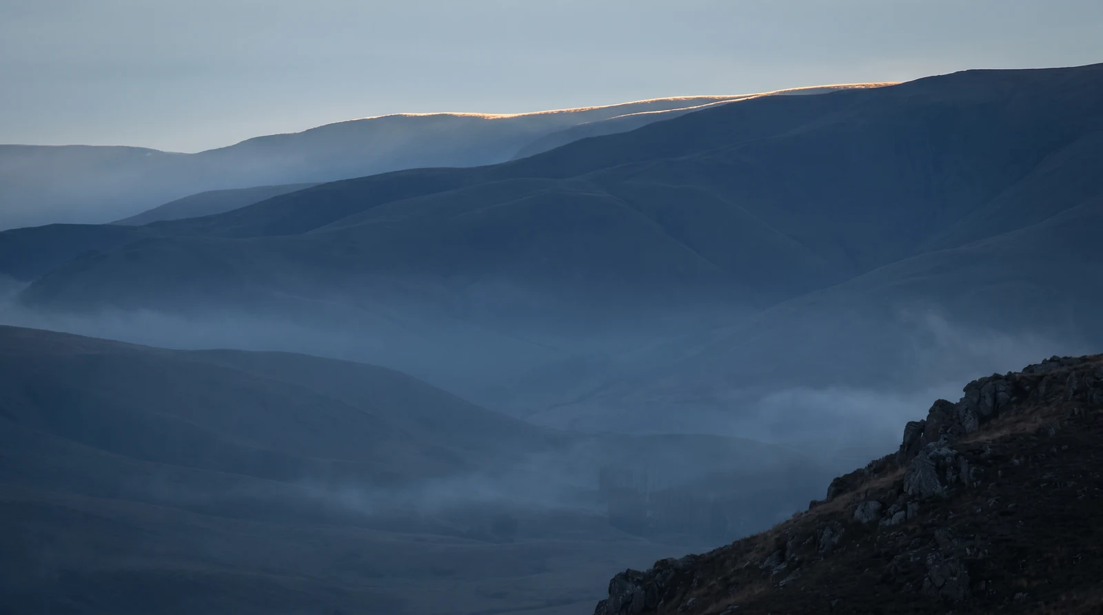 Layered hills in blue haze, with first light along one ridge.